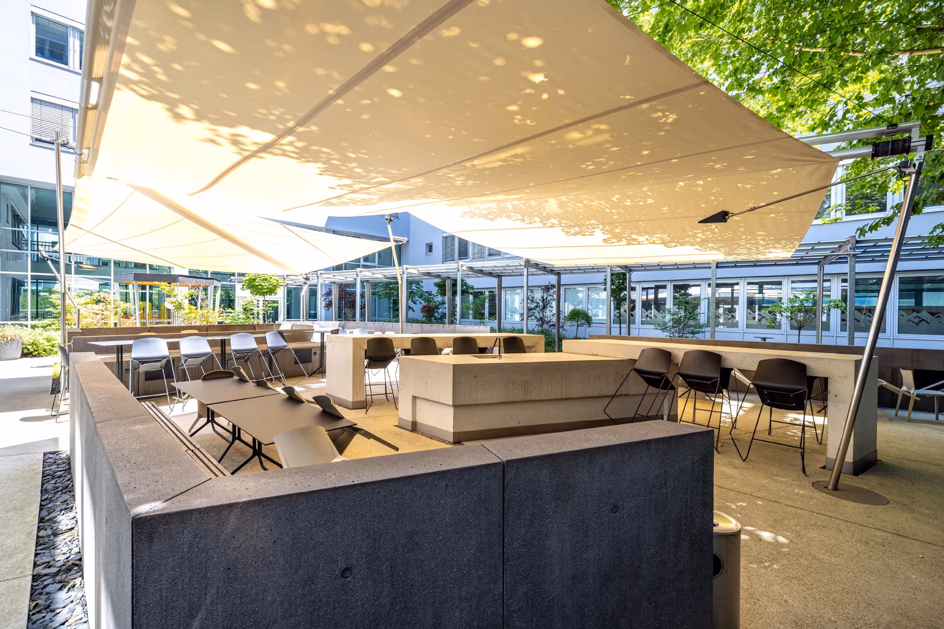 SunSquare® Sonnensegel über modern gestaltetem Innenhof eines Betriebsgebäudes – Schatten für Mitarbeiterbereich