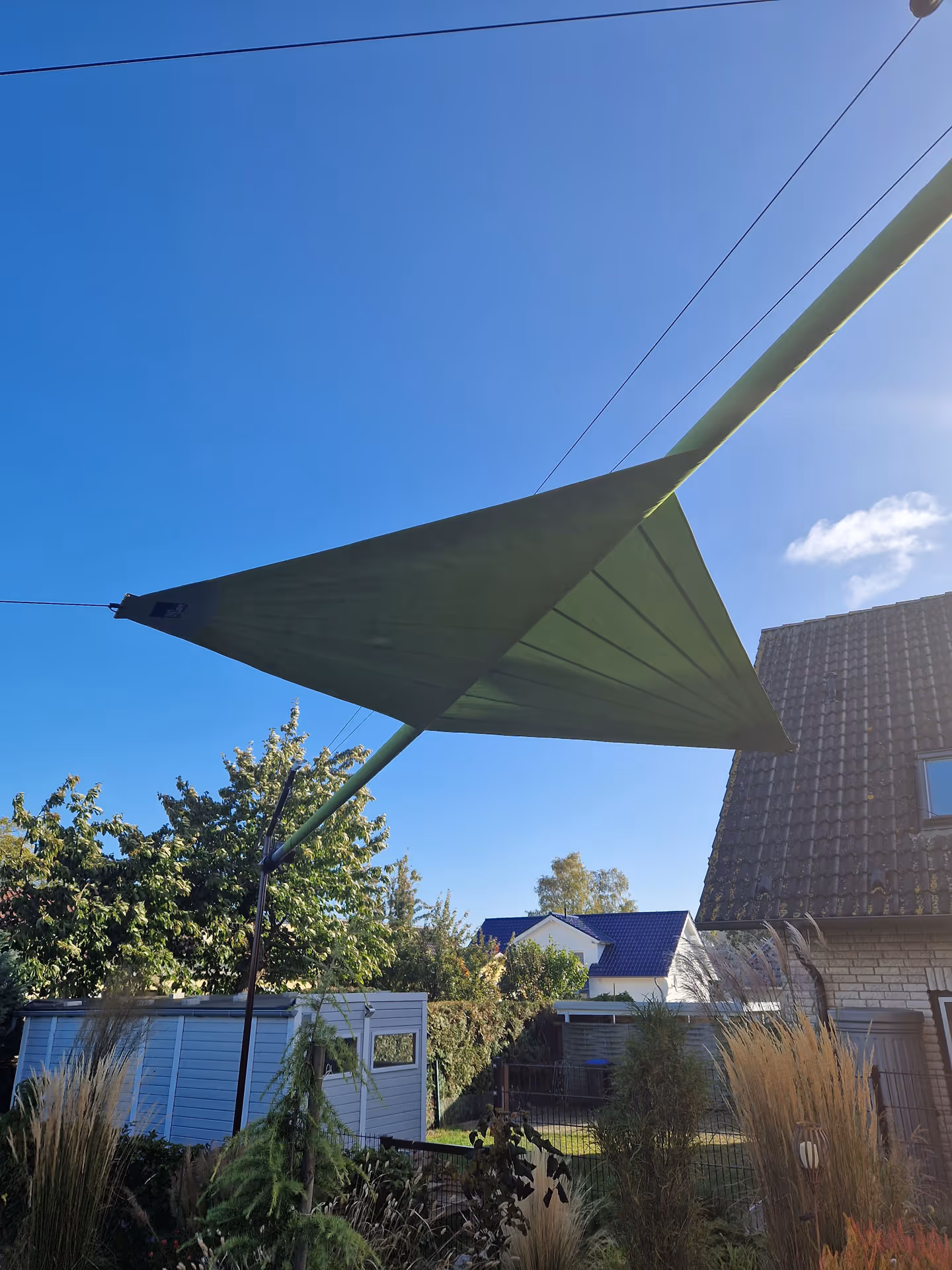 Ein leicht geöffnetes Sonnensegel in grün in einem schönen Garten.