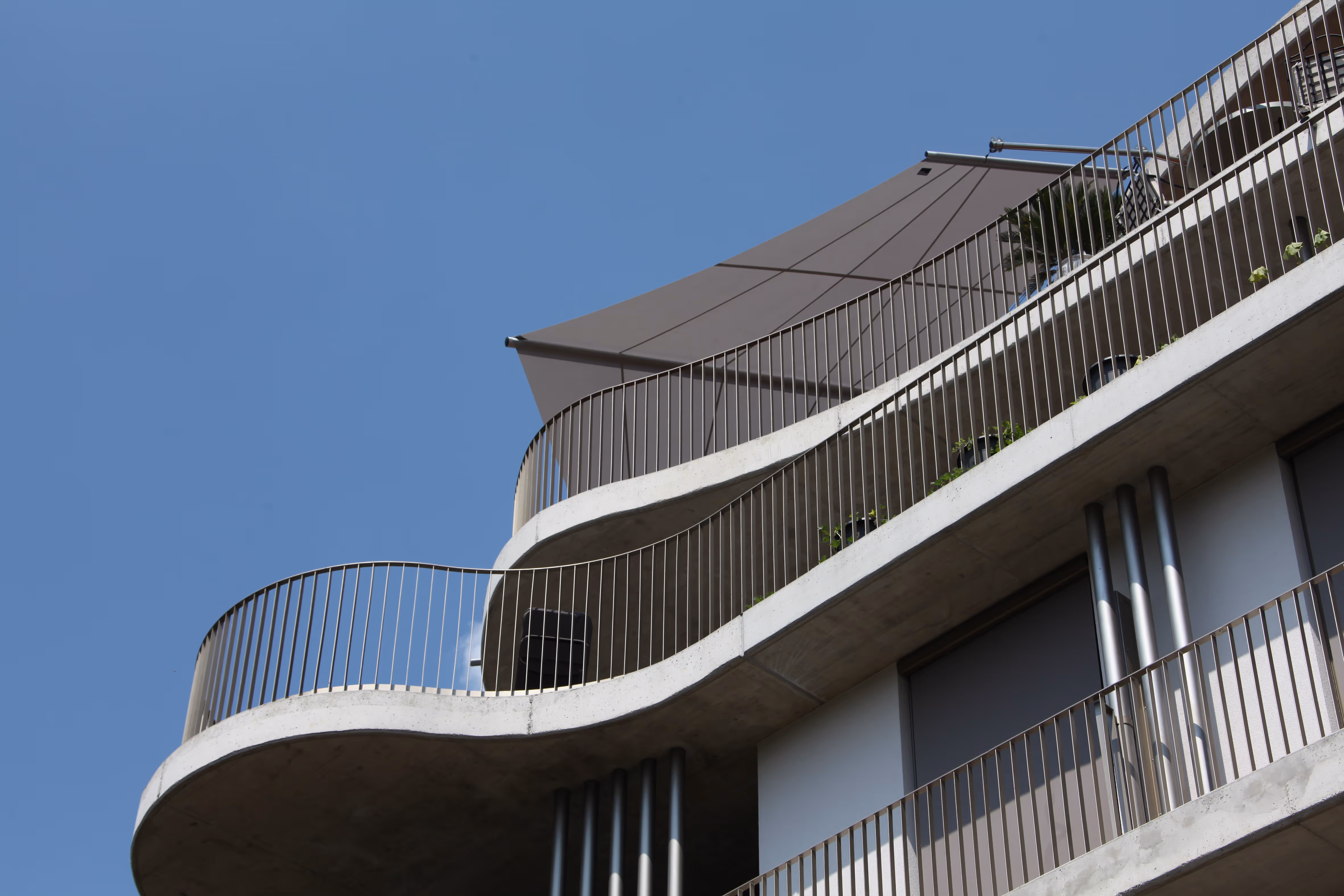 Spacious roof terrace with wooden floors and flower pots with lots of plants with rectangular awning, which prevents the plants from drying out.