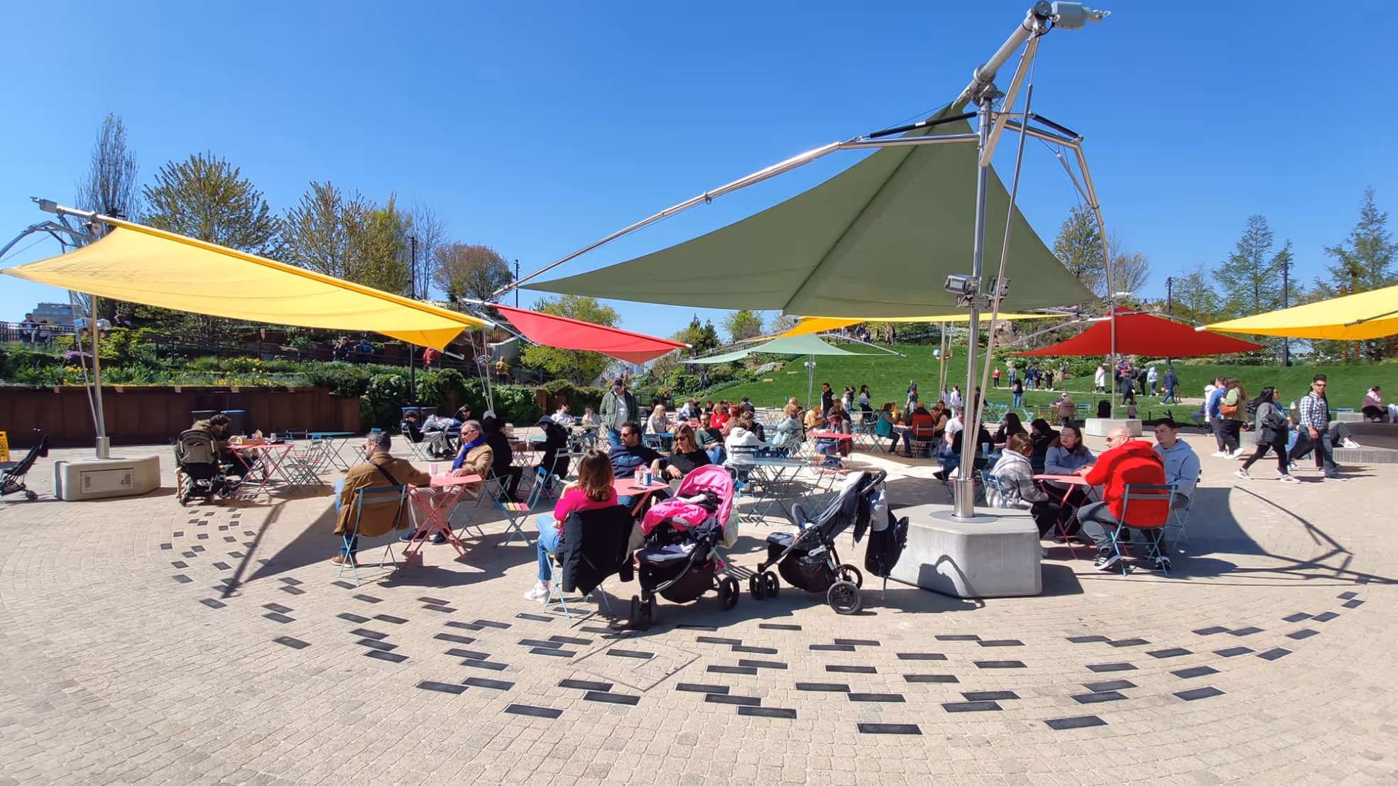 Crowd of peolple relaxing under the sail umbrella FOLD & ROLL by SunSquare at Little Island Park New York.