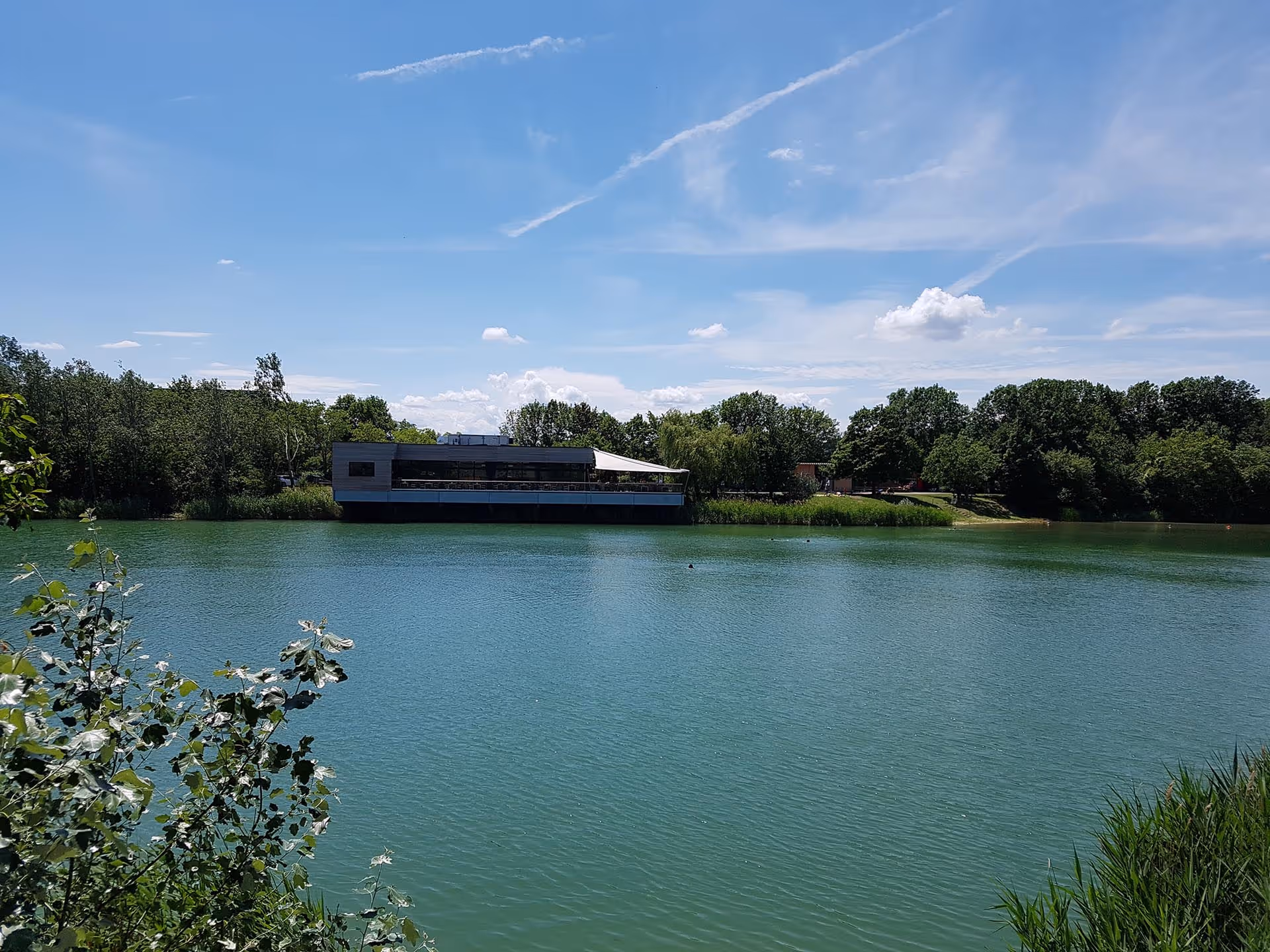 Blick von der Ferne auf die Terrasse des Südufer mit harmonisch integrierten SunSquare Segeln.