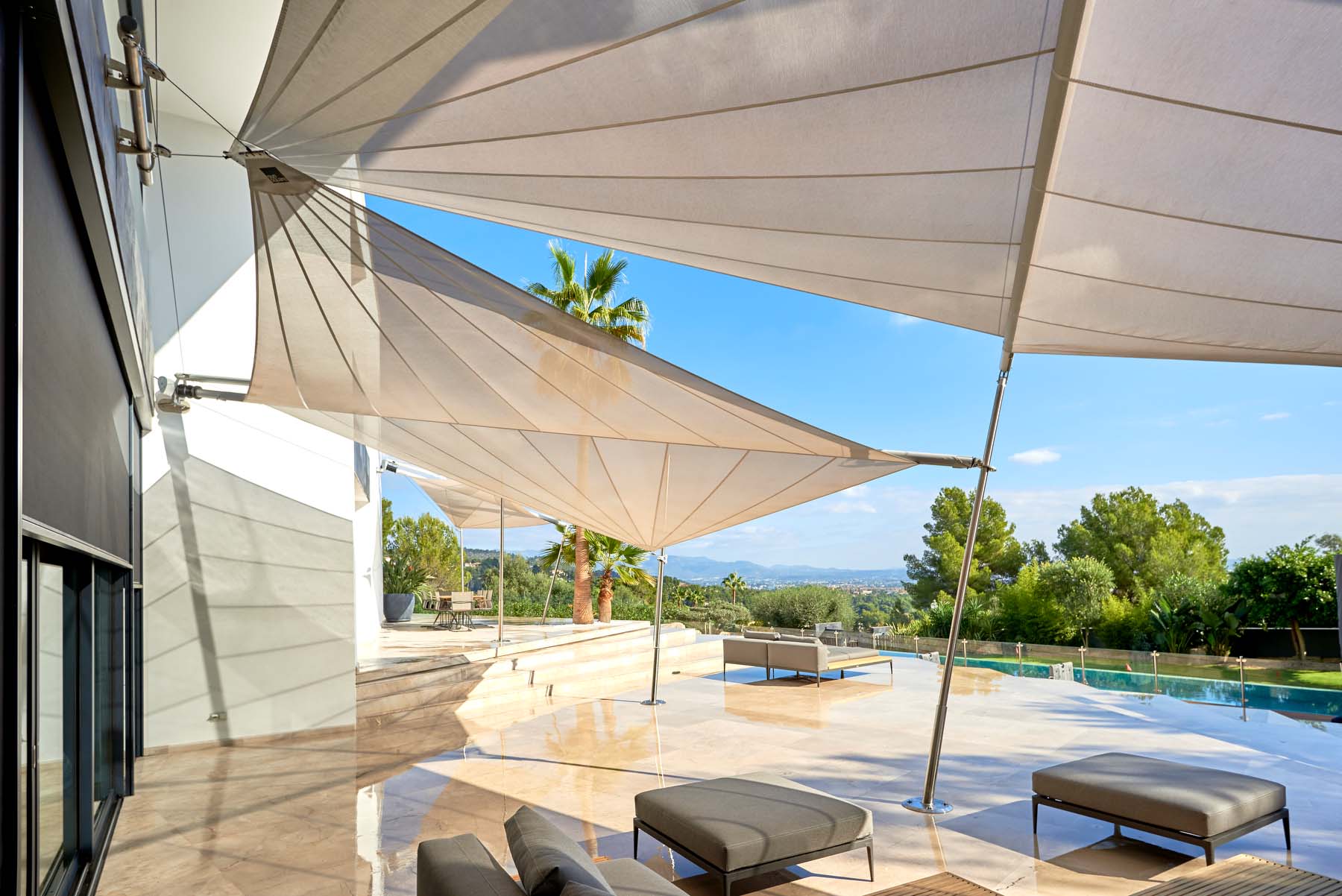 An exclusive villa in Spain with three SunSquare SQK-I sun sails over the pool terrace, seamlessly integrated into the modern architecture with wide views of the surrounding greenery.