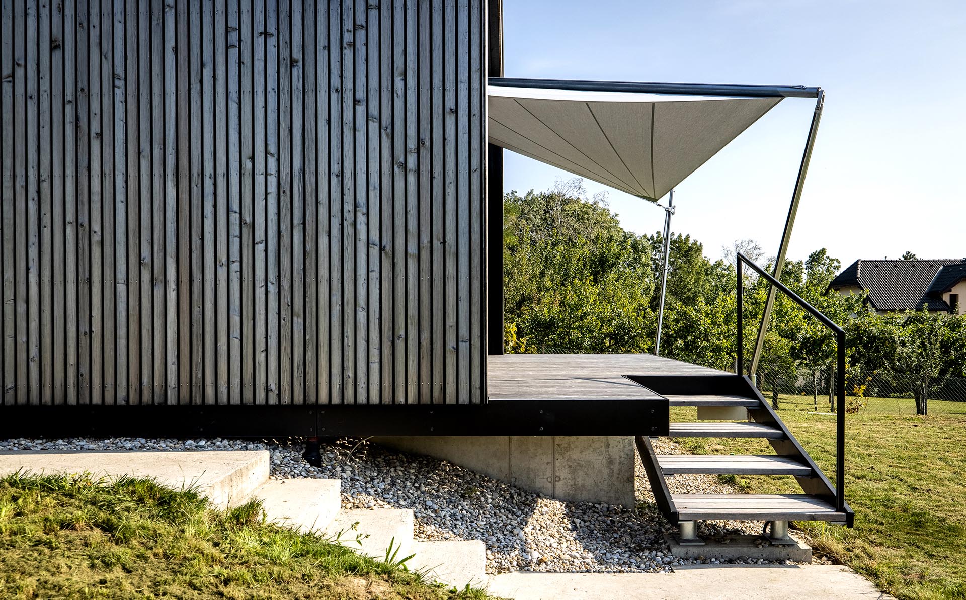 Ansprechende Aufnahme des Gesamtprojekts - die Holzfassade und die vorgezogene Terrasse beschützt von dem SunSquare Segel.