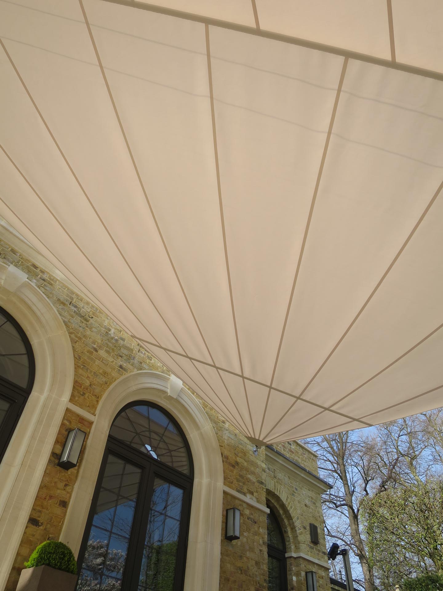 Maßgefertigtes Sonnensegel in Sandfarbe harmoniert mit klassischer Architektur und gepflegter Gartenanlage.