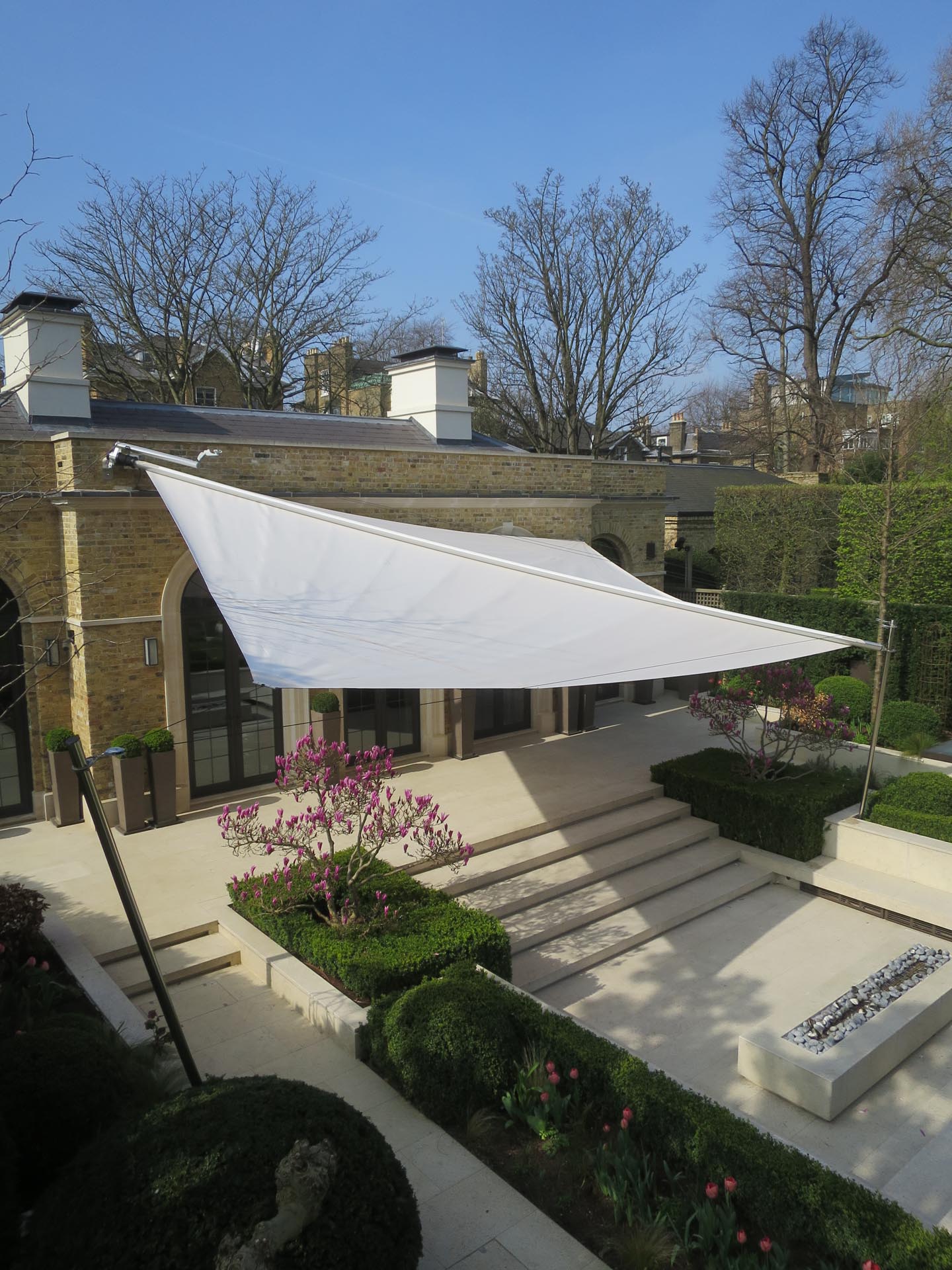 Automatisches SunSquare Sonnensegel schafft großzügigen Schatten über Terrasse und Wohnbereich im Freien.