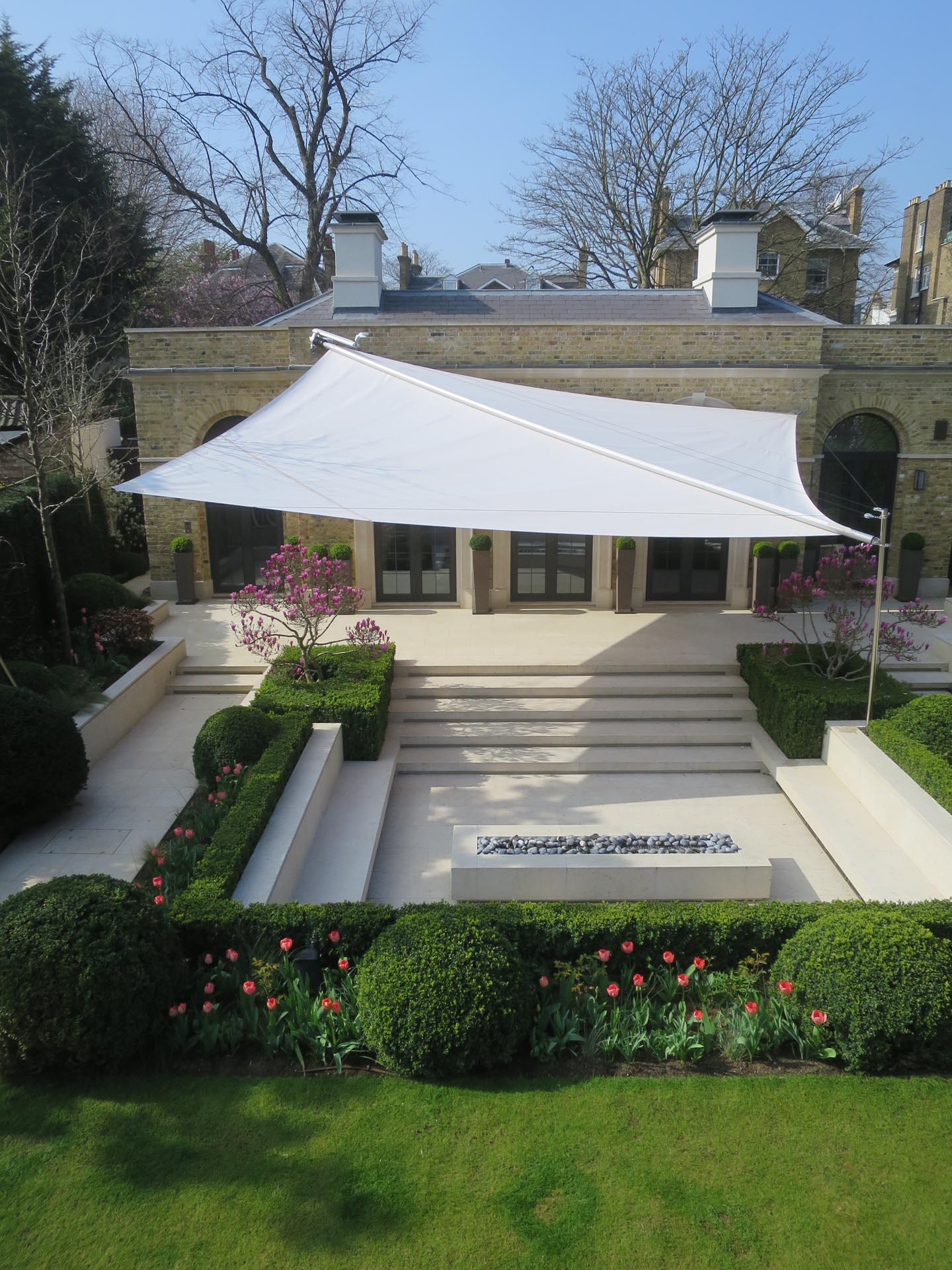 Großflächiges Sonnensegel über Terrasse und Garten schafft komfortablen Outdoor-Wohnraum.