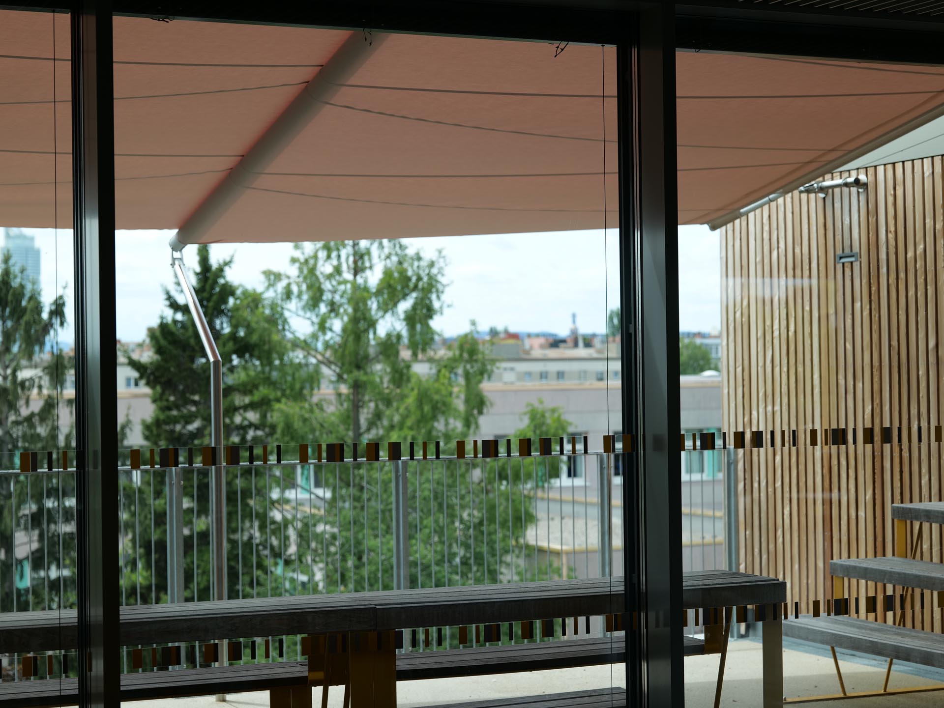 Blick von Innen nach Außen auf die Terrassenfläche, die das große Rechtecksegel beschattet und schützt.