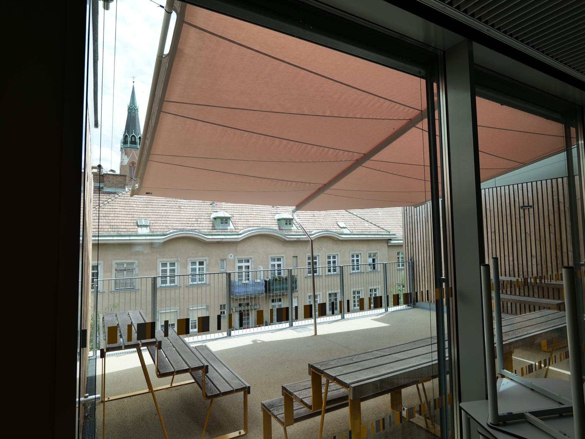 Blick von Innen nach Außen auf die Terrassenfläche, die das große SunSquare Rechtecksegel beschattet und schützt.