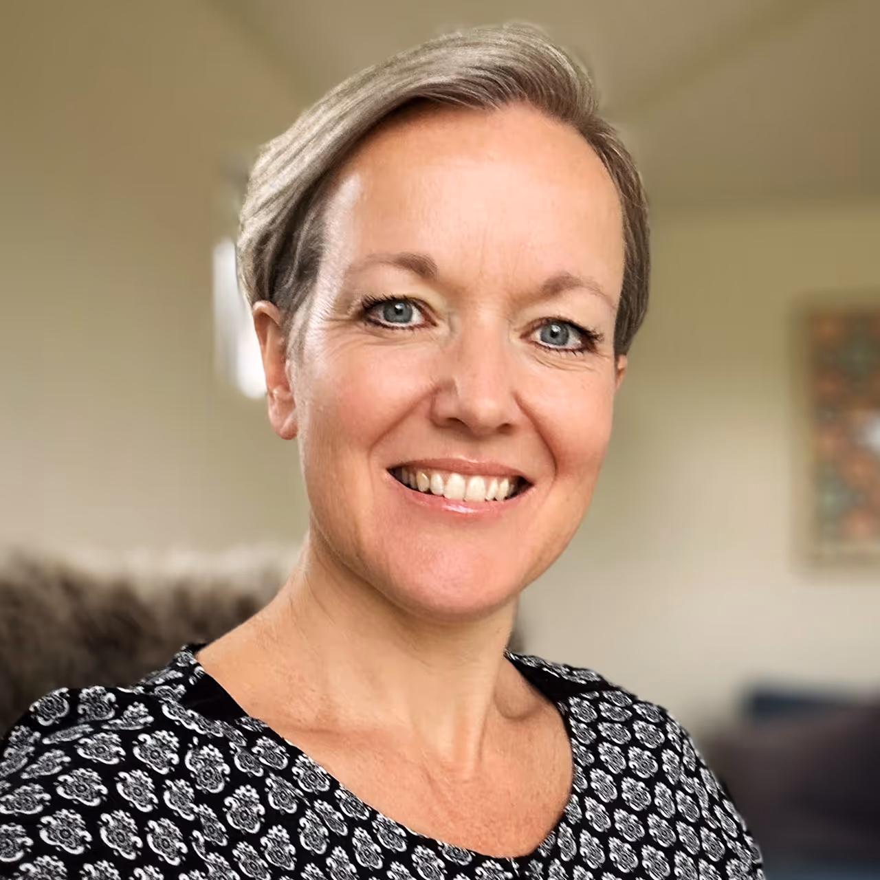 A portrait picture of a caucasian woman looking into the camera, smiling, with a blurry background.