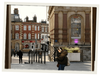 A pedestrian street lined with historical architecture, with people walking and a woman in a winter coat using her phone in the foreground.