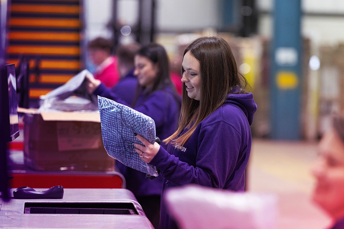 Woman in a purple hoodie scanning packaged clothing at a warehouse checkout counter.
