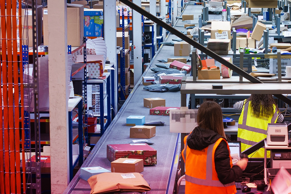 Workers in safety vests sorting packages on a conveyor belt in a warehouse.