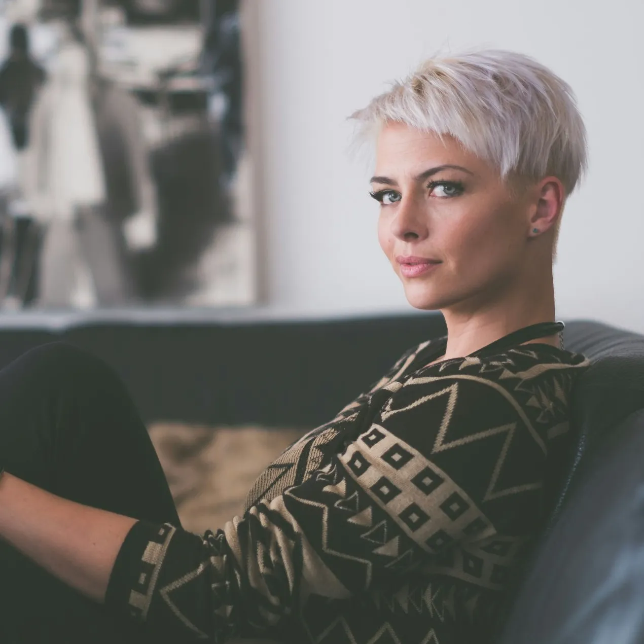 Woman with short platinum hair sitting on couch in geometric patterned sweater