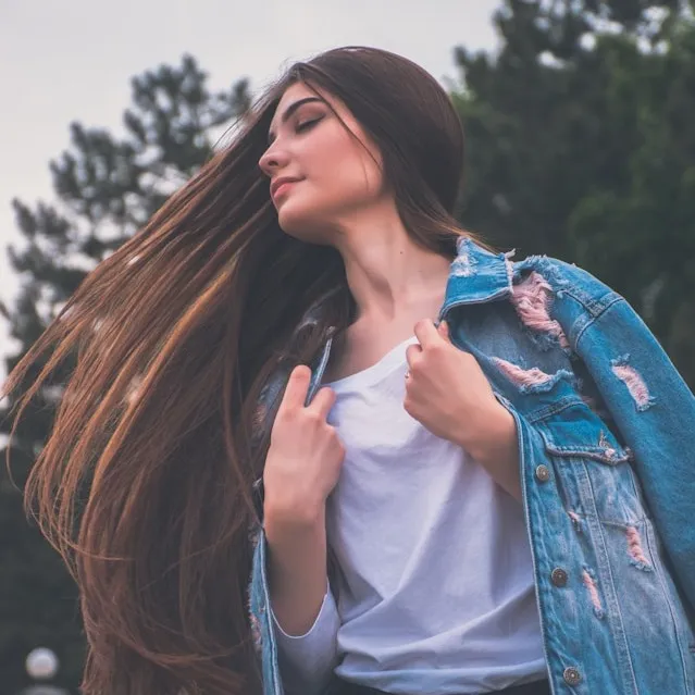 Woman with flowing hair in distressed denim jacket enjoys peaceful moment outdoors