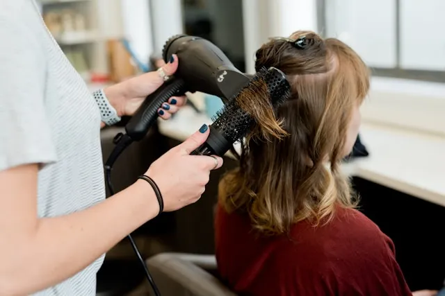 Hairstylist blow-drying and styling woman's hair in salon