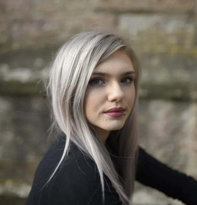 Young woman with silver-blonde hair looking sideways against stone wall