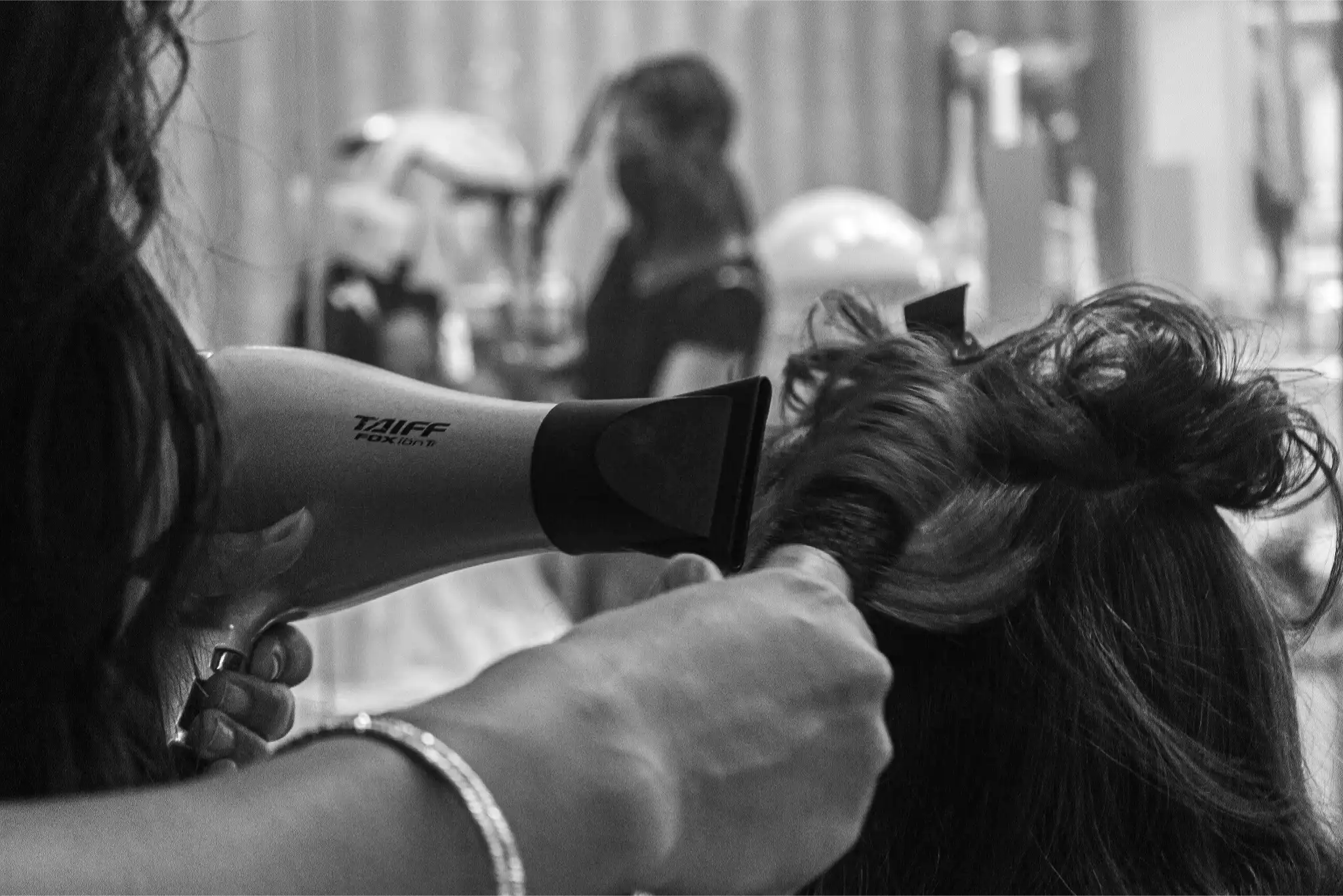 Hairstylist using Taiff hairdryer to style long dark hair in salon