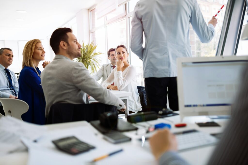 Group of professionals engaged in a meeting, listening attentively to a speaker presenting strategies for accountability and leadership development in a modern office setting.