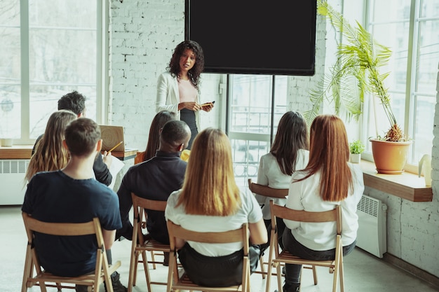 Female African American speaker presenting to small business leaders in a workshop setting, emphasizing leadership training and development, with attendees engaged and seated in a bright, modern classroom.