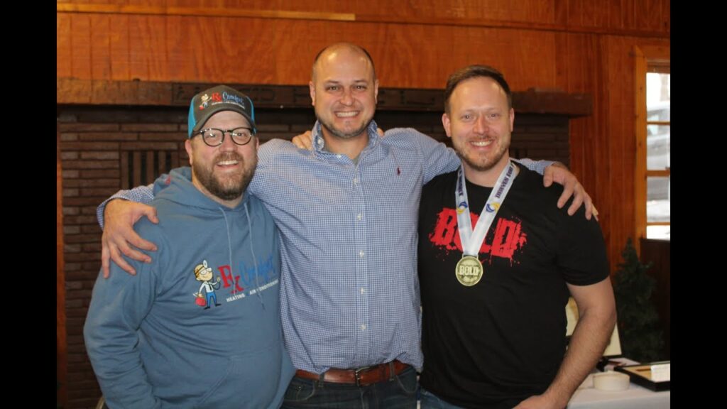 Three men posing together, smiling, in a casual setting; one wearing a medal, representing teamwork and camaraderie in leadership training.