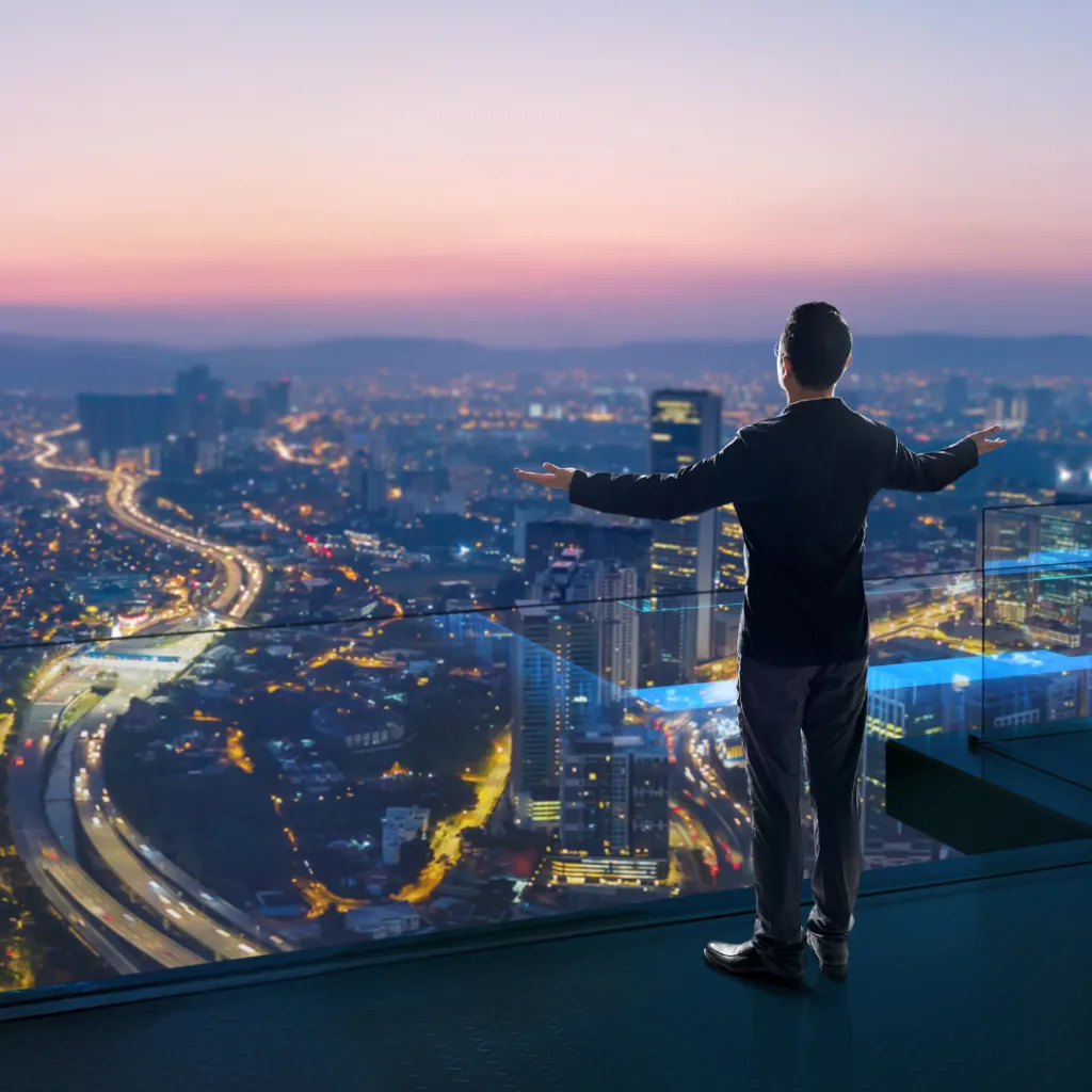 Man in business attire standing with arms open, overlooking a city skyline at dusk, symbolizing visionary leadership and emotional connection in team dynamics.