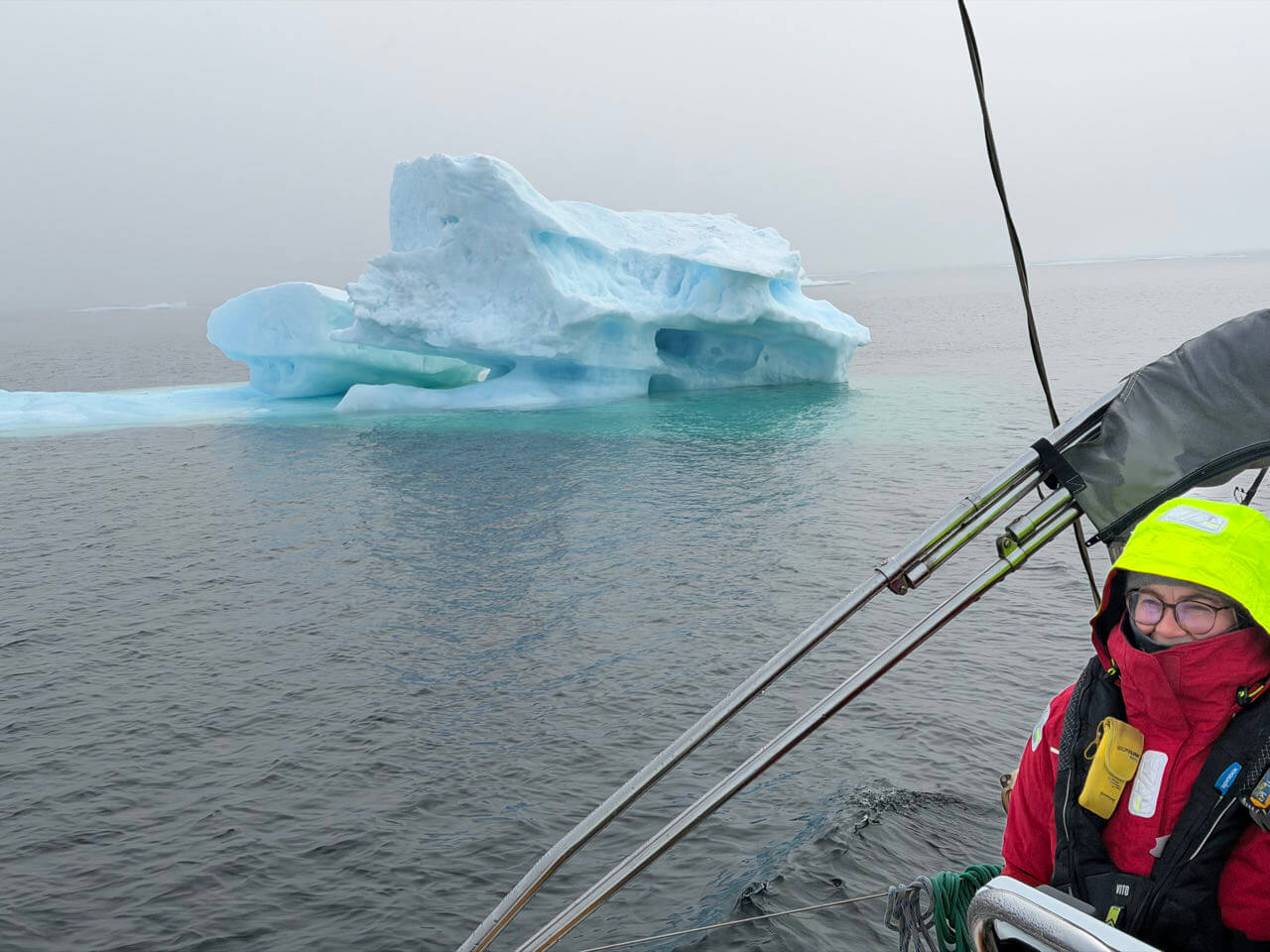 Anne at the helm of Vanuily as the sailboat passes an iceberg during its Northwest Passage voyage.