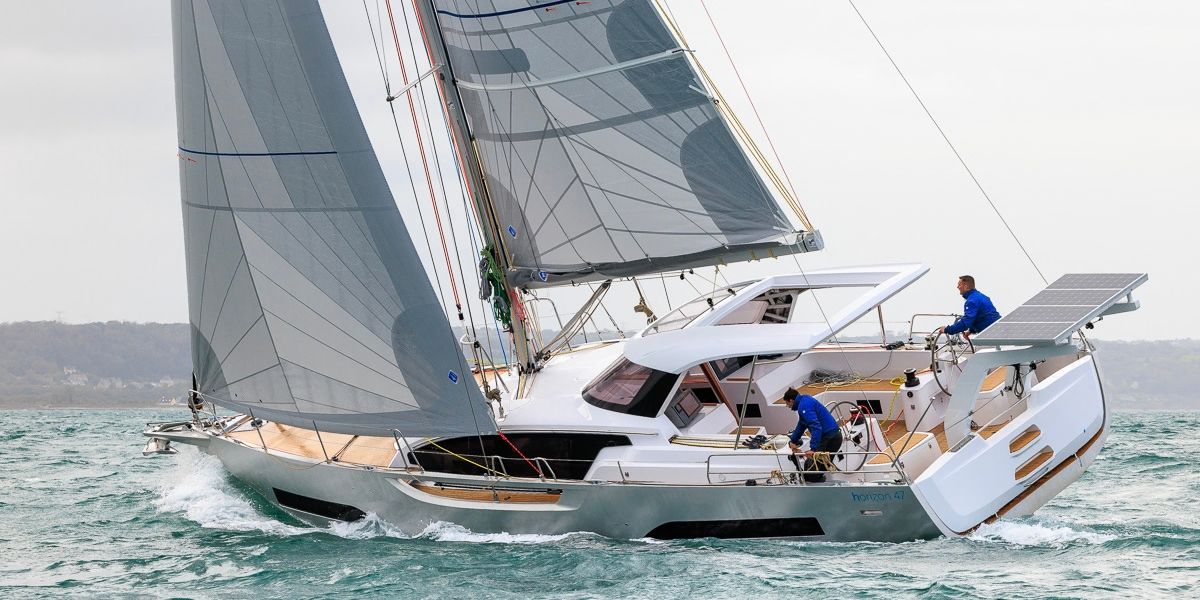 Aft-quarter view of the Allures Horizon 47 under sail, showing the protected cockpit and stern-mounted solar panels.