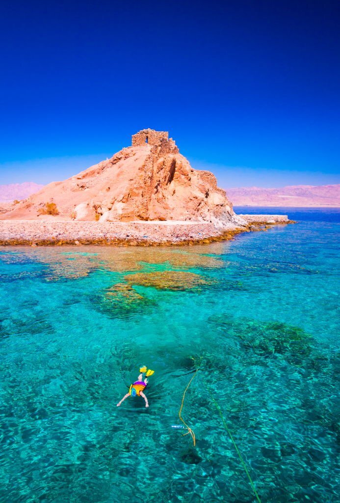 Schnorchler im türkisblauen Wasser vor der Pharaoneninsel bei Taba, Ägypten – mit Blick auf die historische Festung auf dem Felsen und das Rote Meer im Hintergrund.