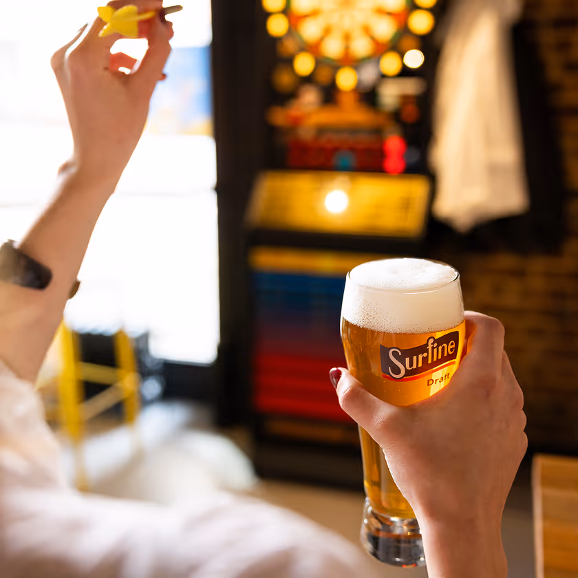 Person tenant un verre de bière Surfine et une fléchette avant un jeu de fléchettes.