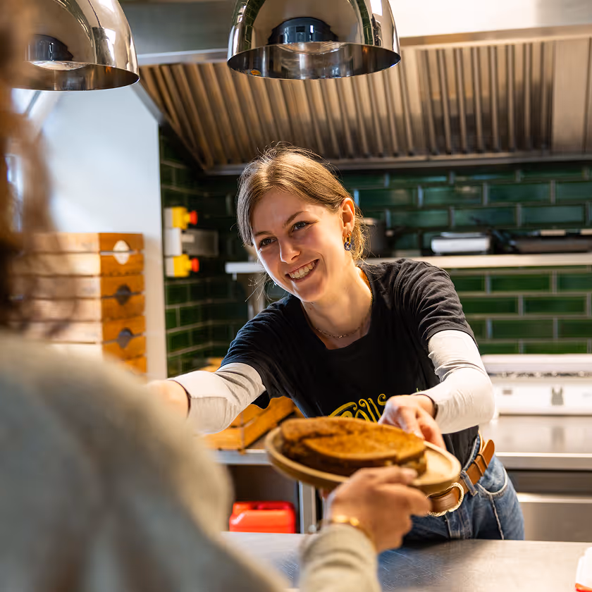 Serveuse souriante tend une assiette avec une tarte à une cliente dans un café moderne.