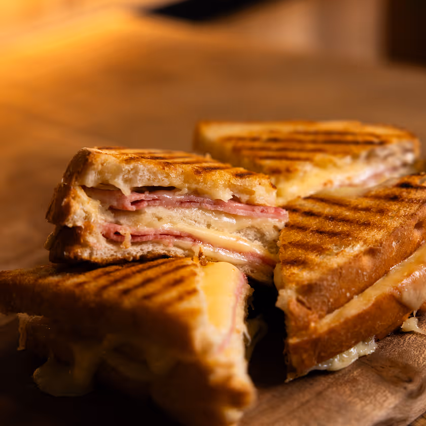 Sandwichs grillés coupés en quartiers avec jambon et fromage fondant sur planche en bois.