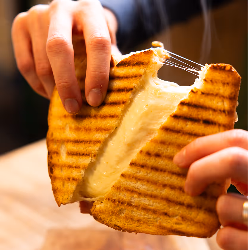 Personnes tenant un sandwich grillé avec fromage fondu filant à l'intérieur.