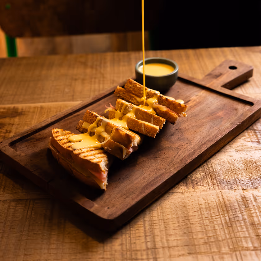 Fromage fondu versé sur des tranches de sandwich grillé posées sur une planche en bois.