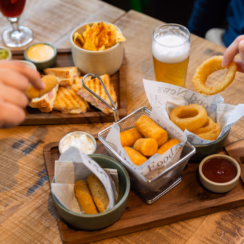 Repas avec onguets de mozzarella, beignets d'oignon, sandwichs grillés, sauces et une bière blonde