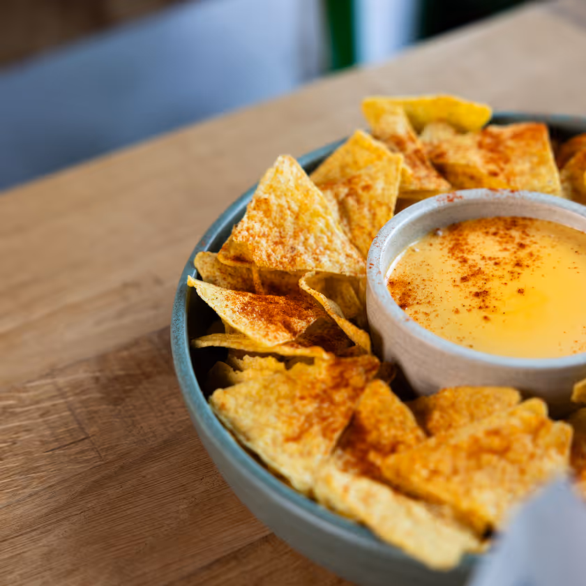 Bol de chips tortilla assaisonnées avec un bol de sauce au fromage saupoudrée de paprika.