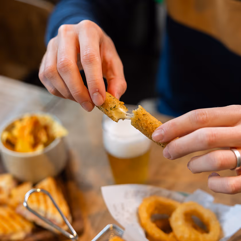 Mains rompent un bâtonnet de mozzarella frit au fromage filant avec des rondelles d'oignon et une boisson.
