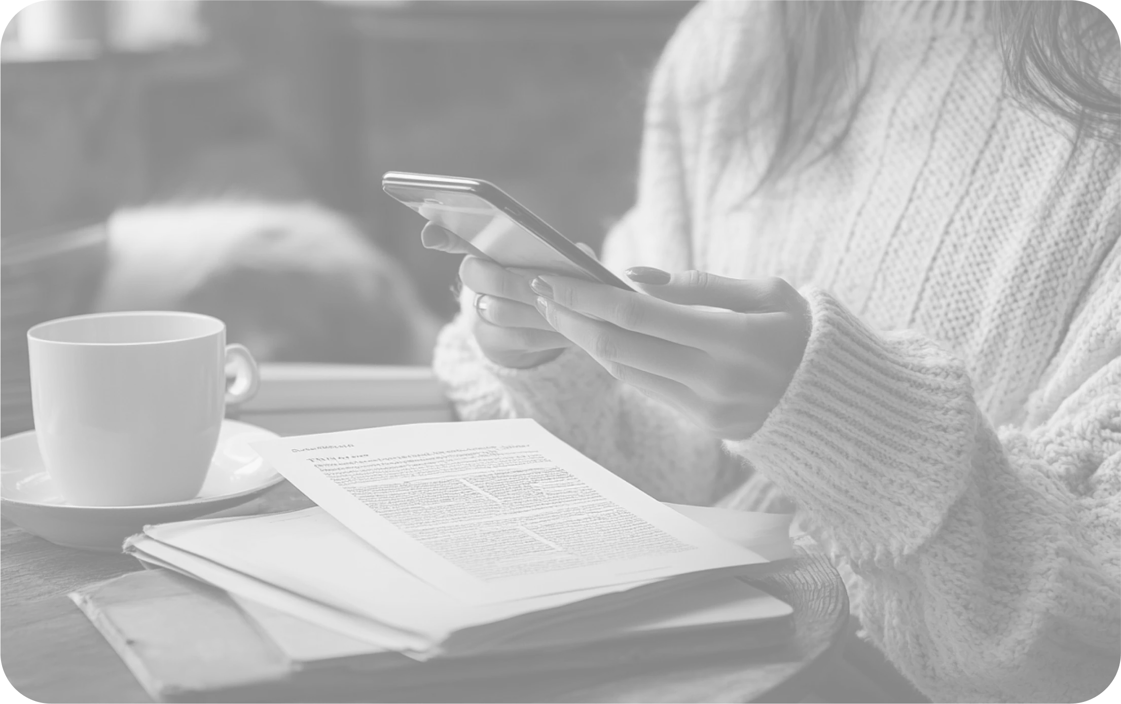 Woman reading news on phone next to a cup and printed paper at a cozy table.