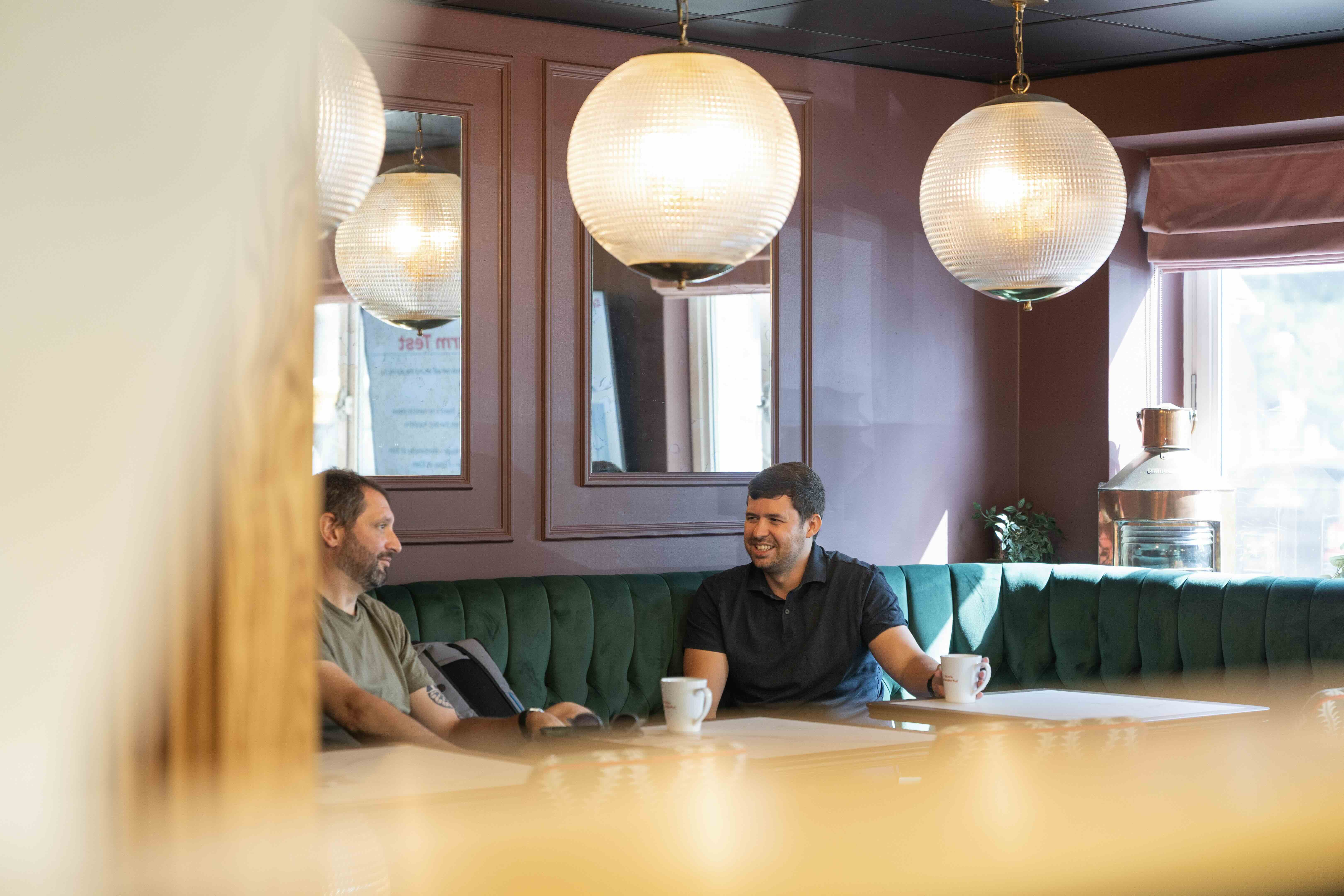 Member chatting over coffee in a green velvet booth in one of DeskLodge's breakout spaces