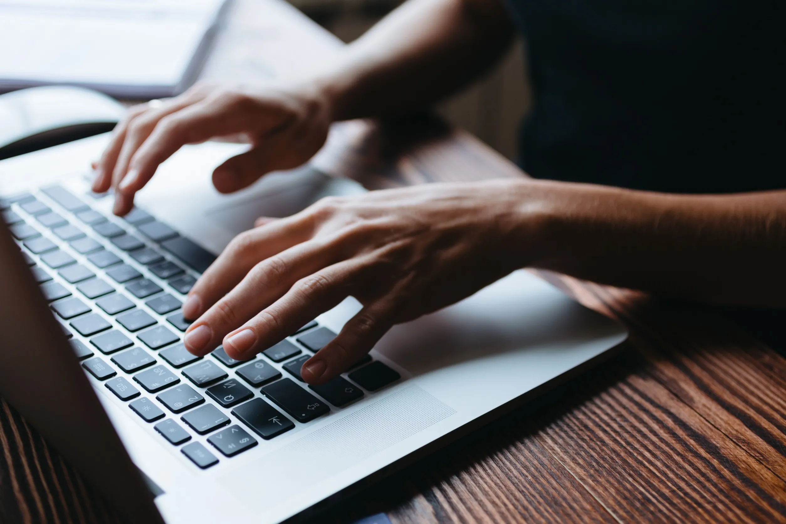 A person typing on a laptop on a wooden table
