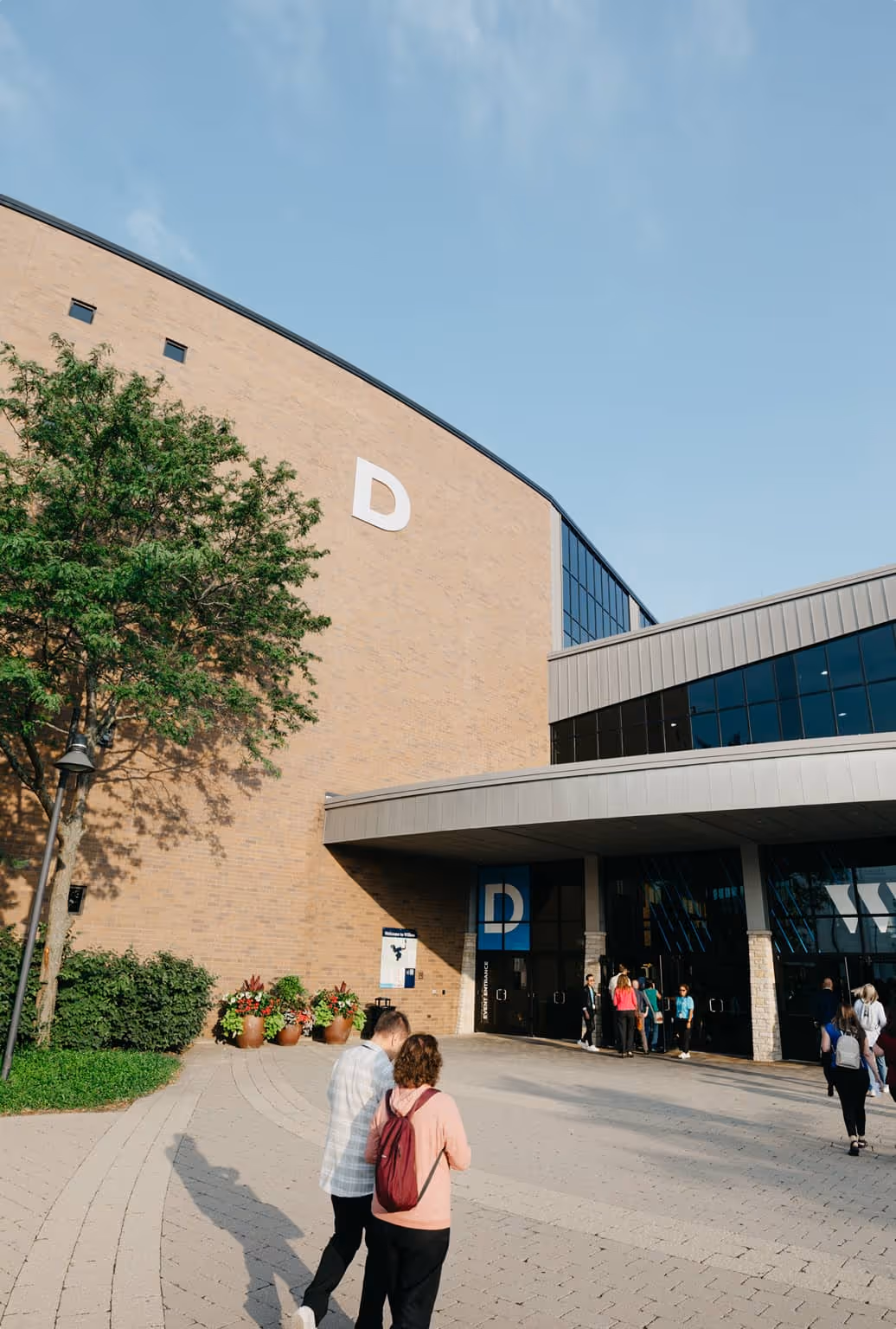 A large group of people walking into the event entrance of large brick building.