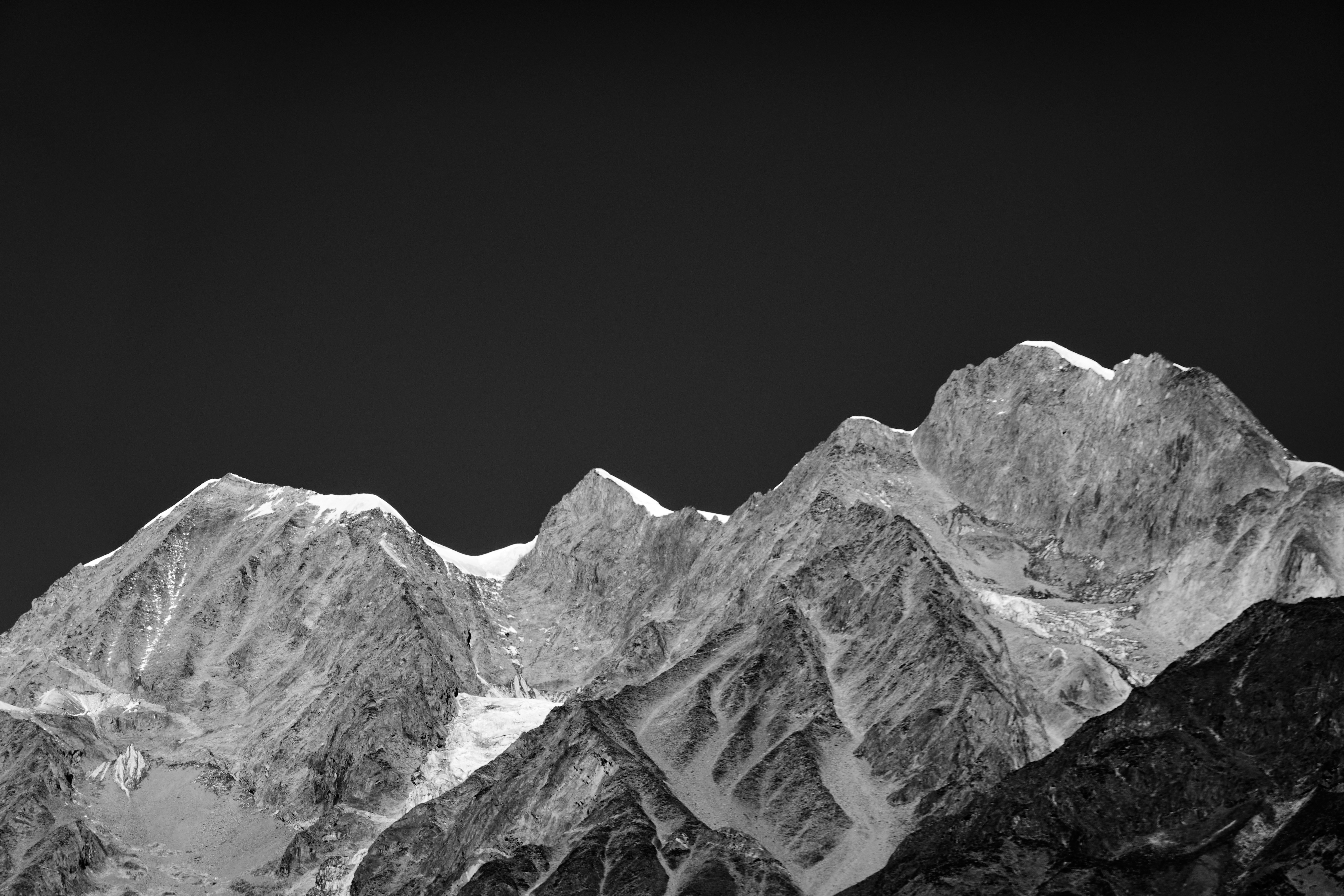 Black and white photo of rugged mountain peaks with patches of snow under a dark sky.