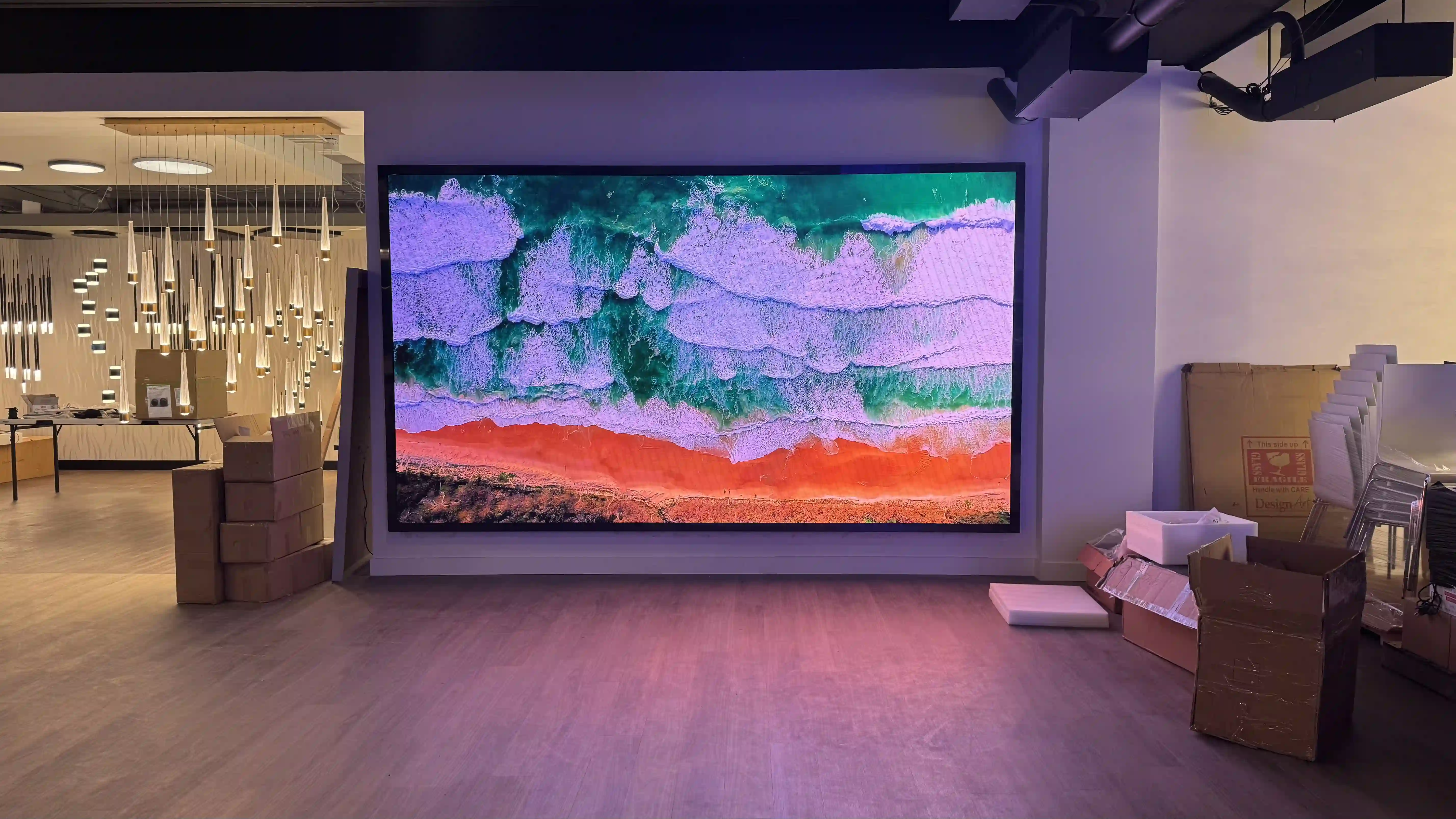 High-resolution LED wall displaying a vivid aerial beach scene, located in a modern lighting showroom with decorative hanging fixtures.
