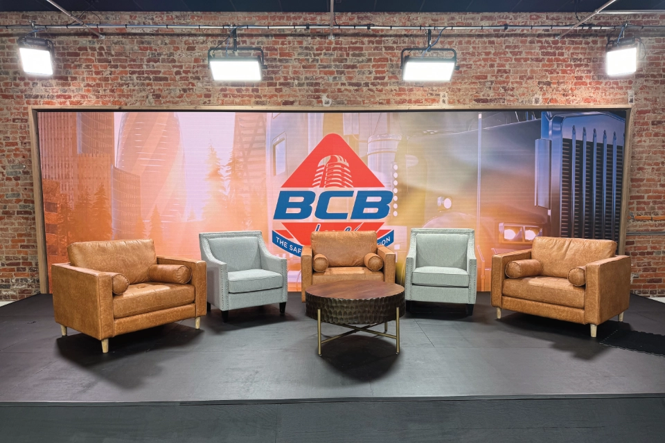 Broadcast studio set with a wide LED video wall displaying the BCB Live logo behind a set of leather and fabric armchairs arranged for a talk show format.