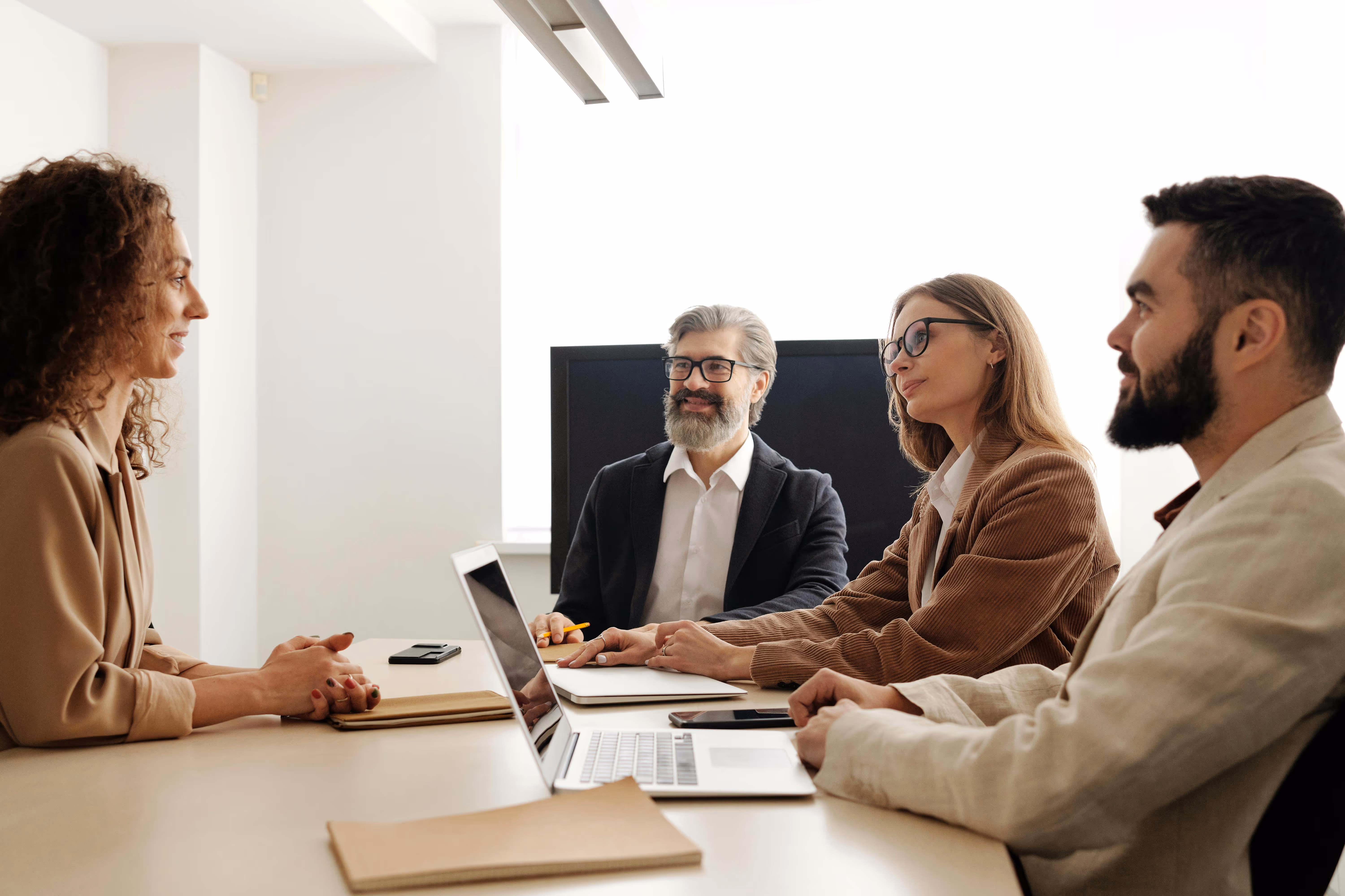 Four business professionals conducting a panel interview in a bright modern meeting room with laptops and notepads