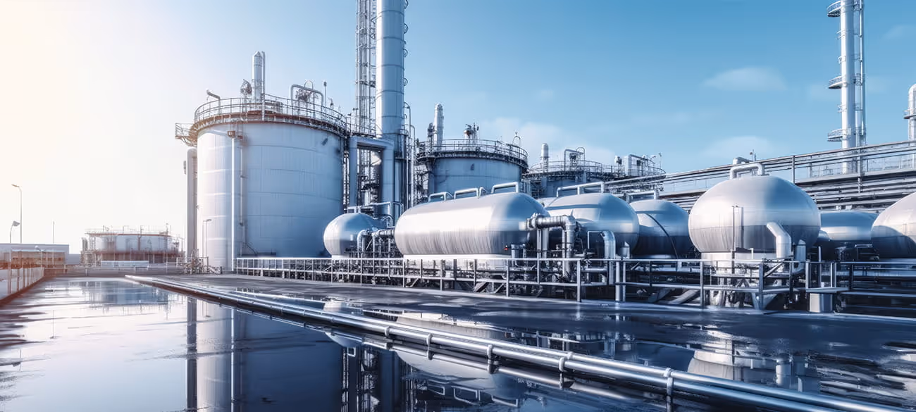 Industrielle Anlage mit großen silbernen Lagertanks und Rohrleitungen unter blauem Himmel.