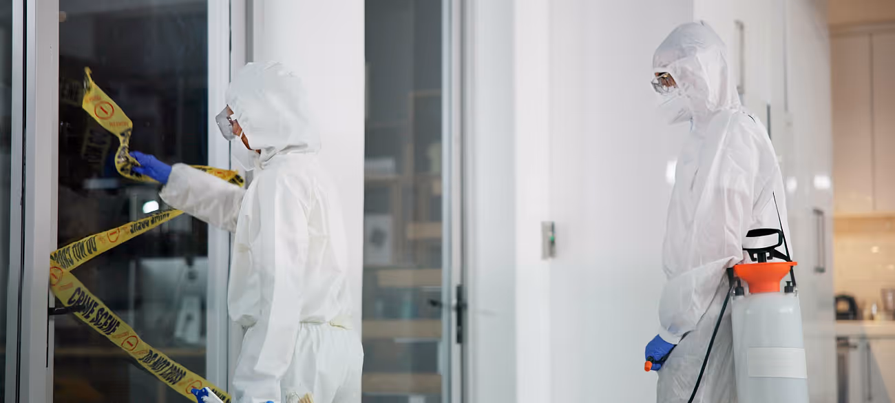Zwei Personen in Schutzanzügen und Handschuhen sichern mit gelbem Absperrband einen Tatort.