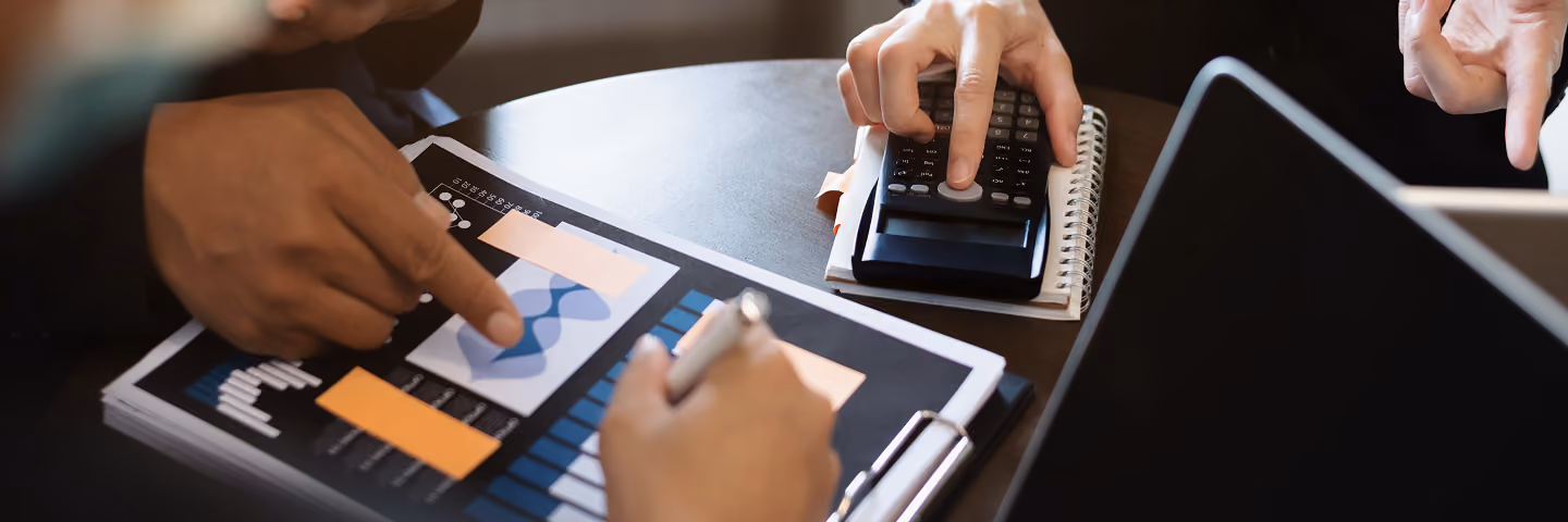 Hands using a calculator beside a notebook and tablet during a financial review