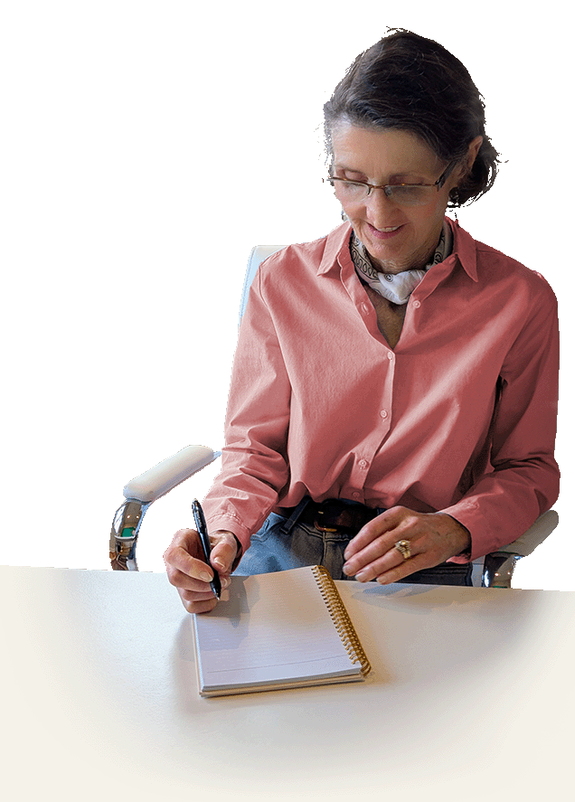 Author Caryn McCann siting on a desk and writing in a notebook.