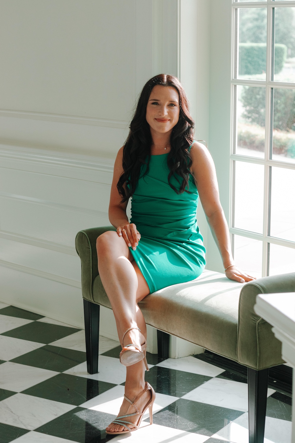 Professional photo of Julia Nista sitting on a bench with a tile floor and a white background with a window looking outside.