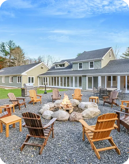 An Image of an Outdoor fire pit with chairs and a large house in the background